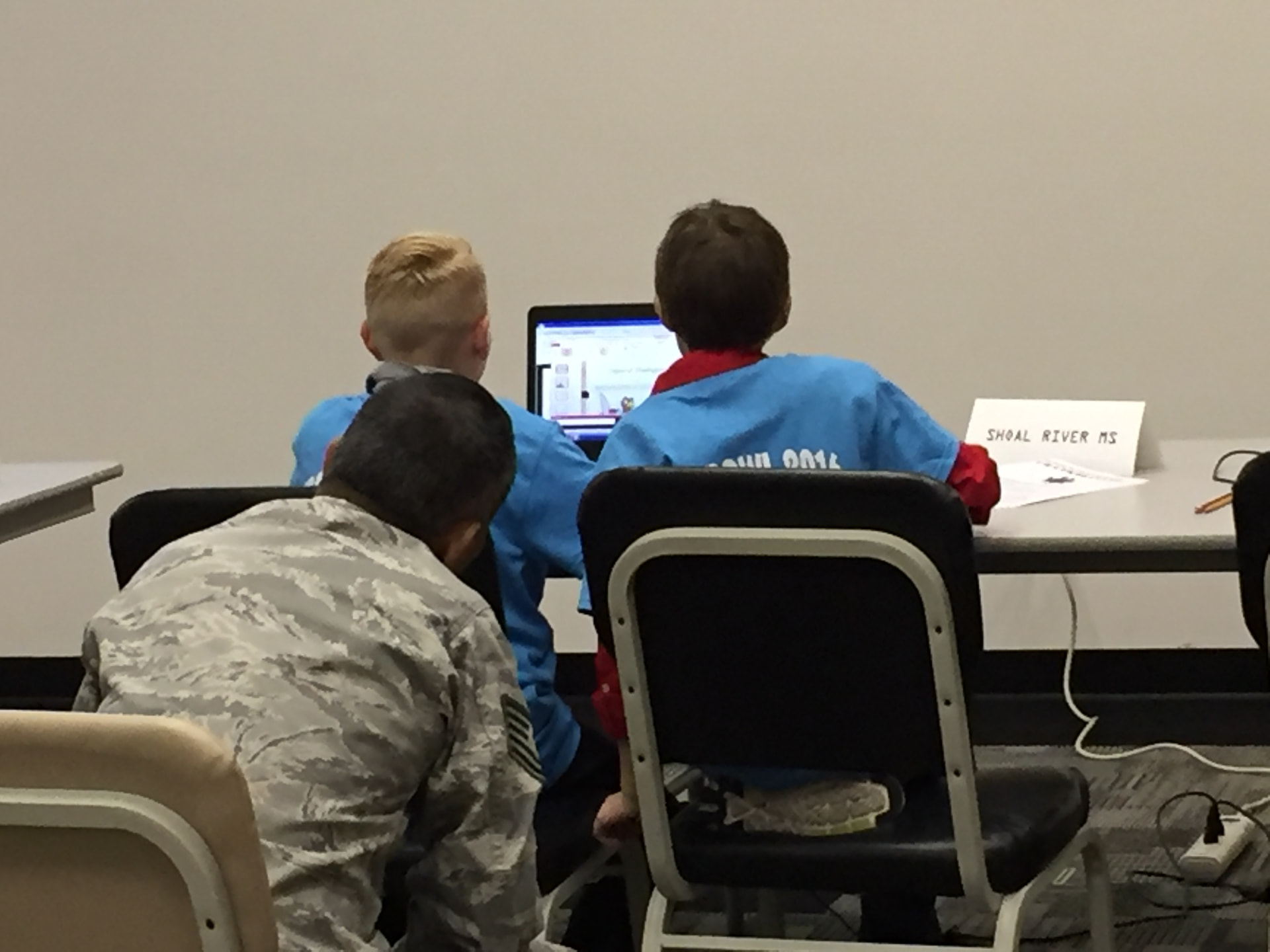 A service member mentoring students at a computer